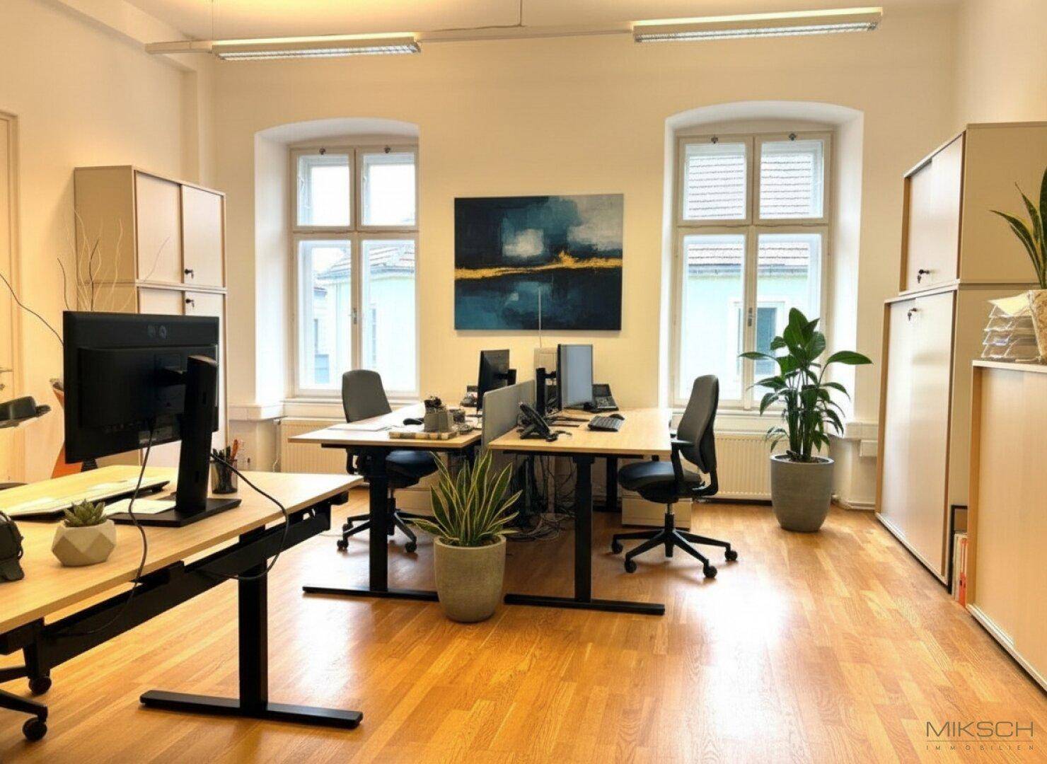 Großzügiges Großraumbüro mit mehreren Arbeitsplätzen, Holzboden und viel natürlichem Licht durch große Fenster.