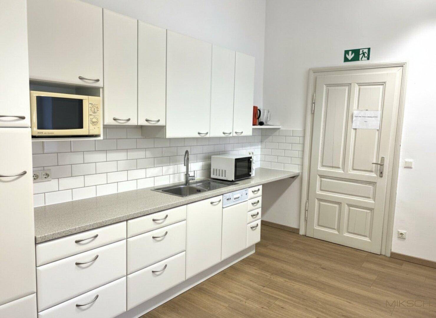 Funktionale Teeküche mit weißen Schränken, Mikrowelle und Spülmaschine, ideal für Büroräume.