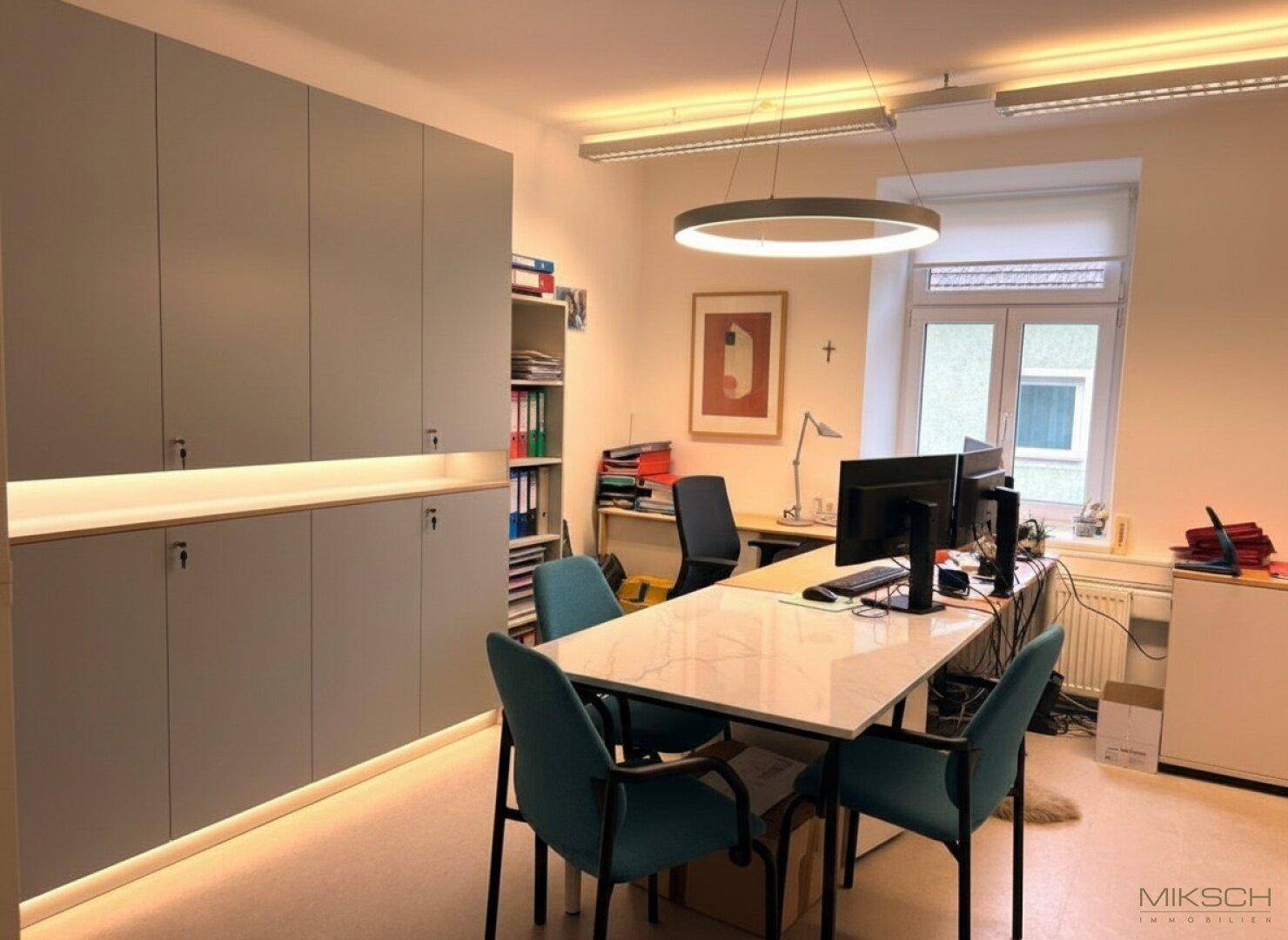 Funktionales Büro mit integrierten Schränken, modernem Beleuchtungsring und einem Besprechungstisch.