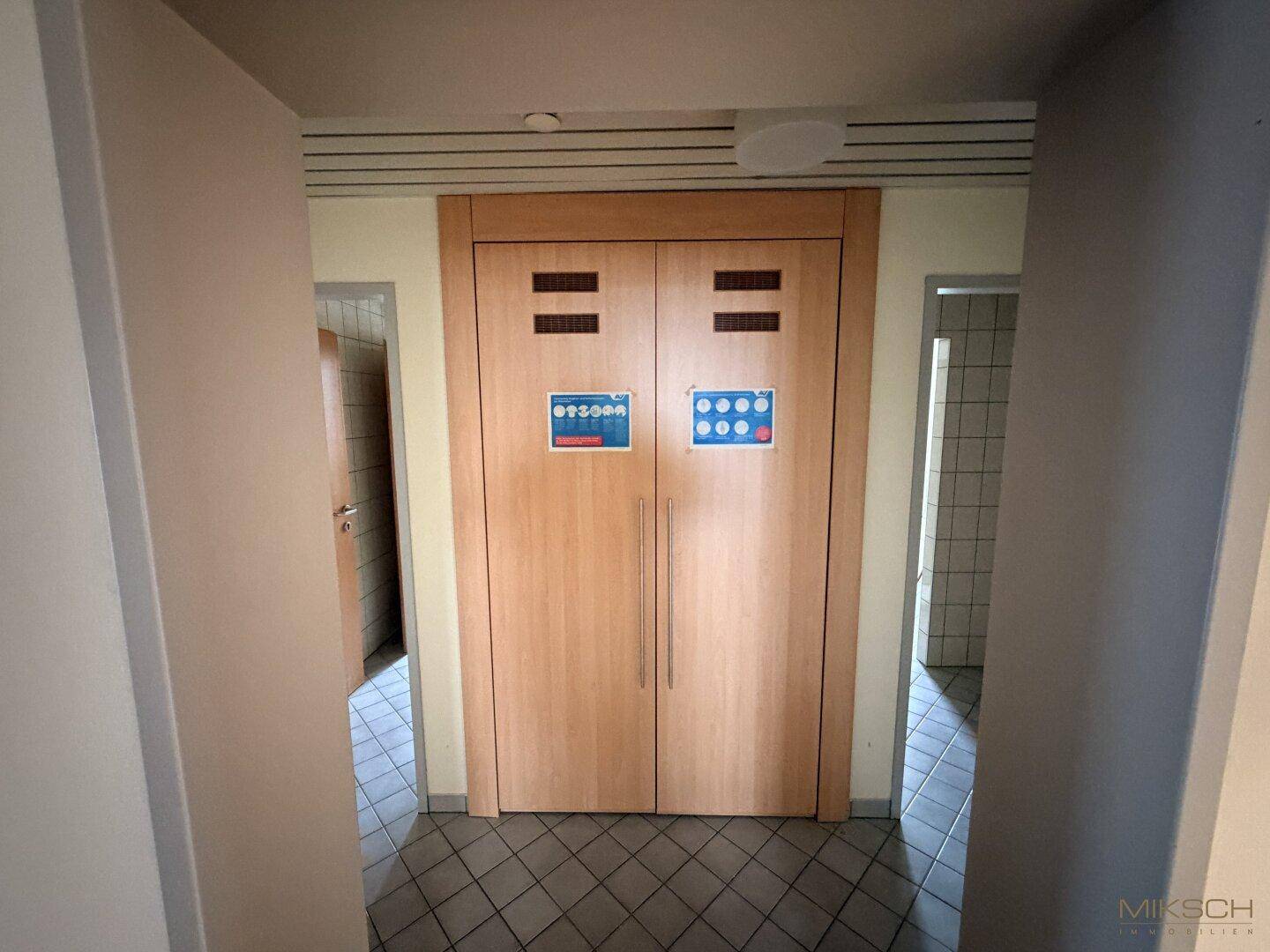 Eingangsbereich zu den Toiletten mit Holztüren und Fliesenboden.
