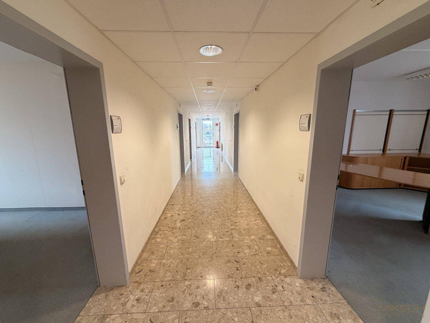 Heller Flur mit Fliesenboden, weißen Wänden und Türen zu verschiedenen Büros.