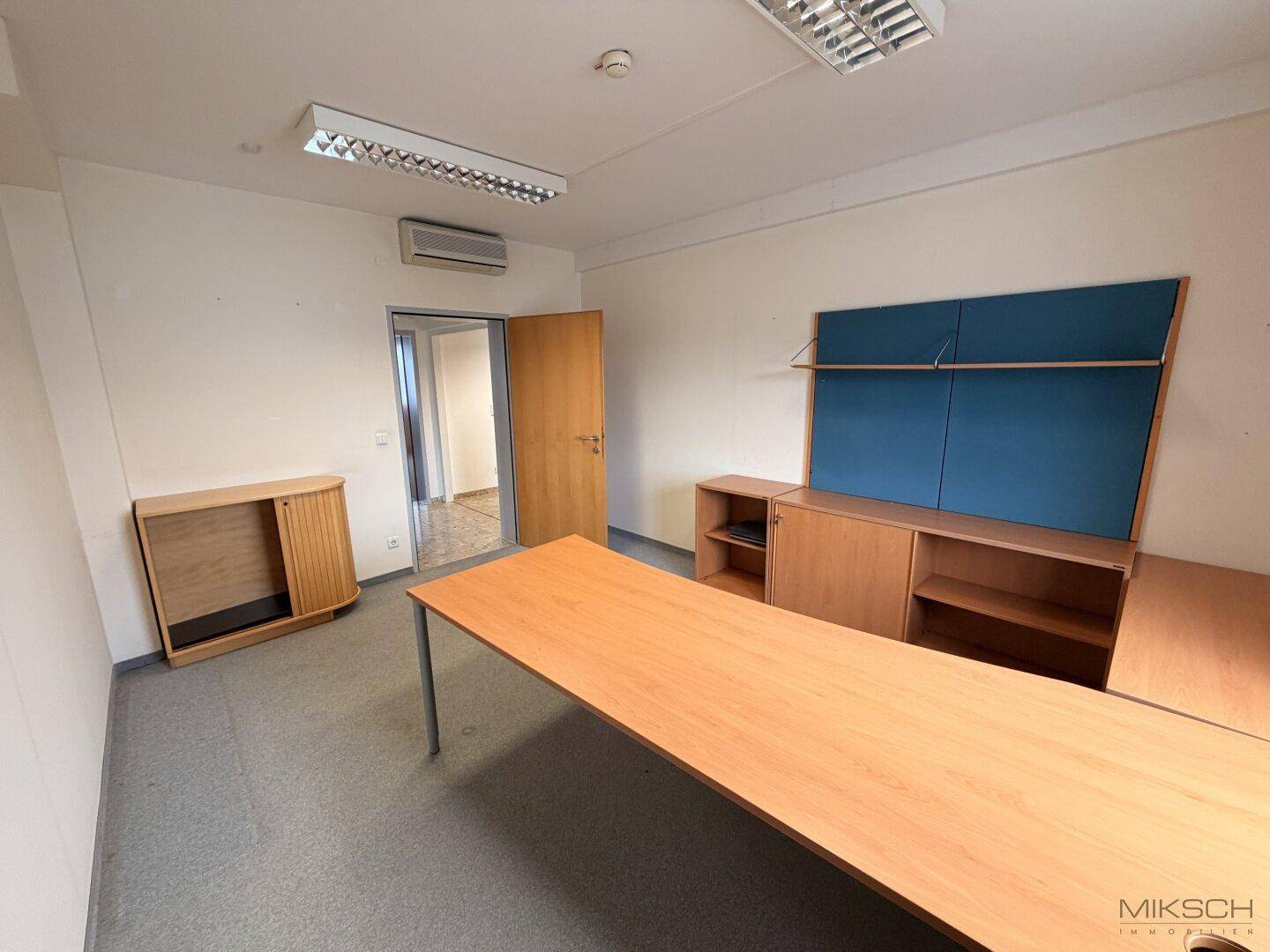 Leeres Büro mit Teppichboden, einem langen Tisch und Schränken, bereit zur individuellen Einrichtung.