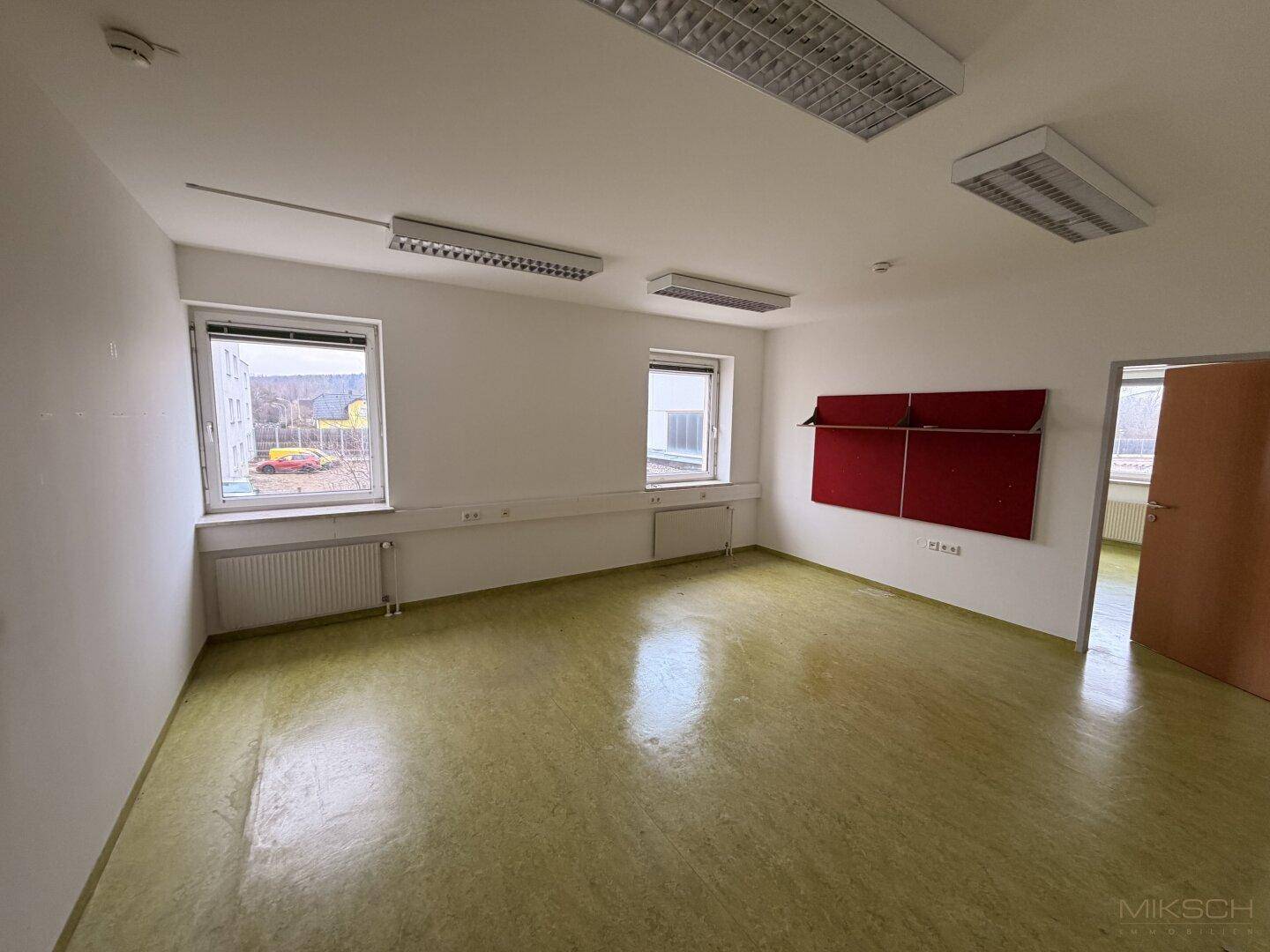 Geräumiger, leerer Raum mit Vinylboden und großen Fenstern, ideal für verschiedene Nutzungen.