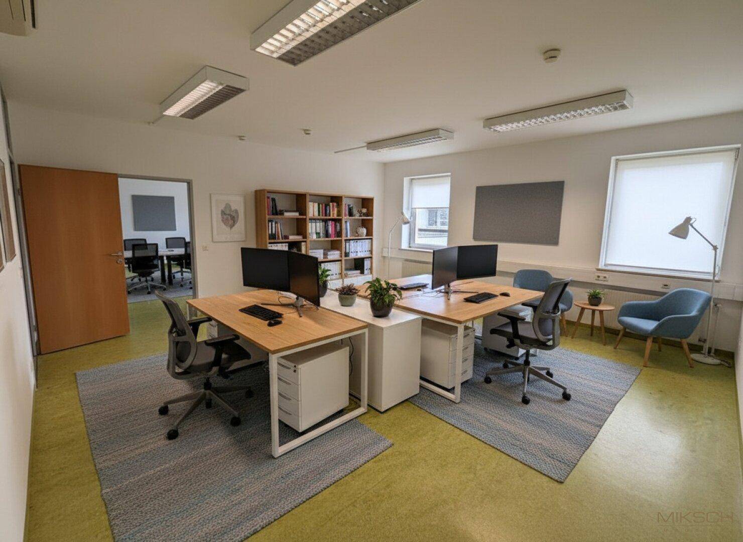 Offener Bürobereich mit mehreren Arbeitsplätzen, grüner Boden und modernen Möbeln.