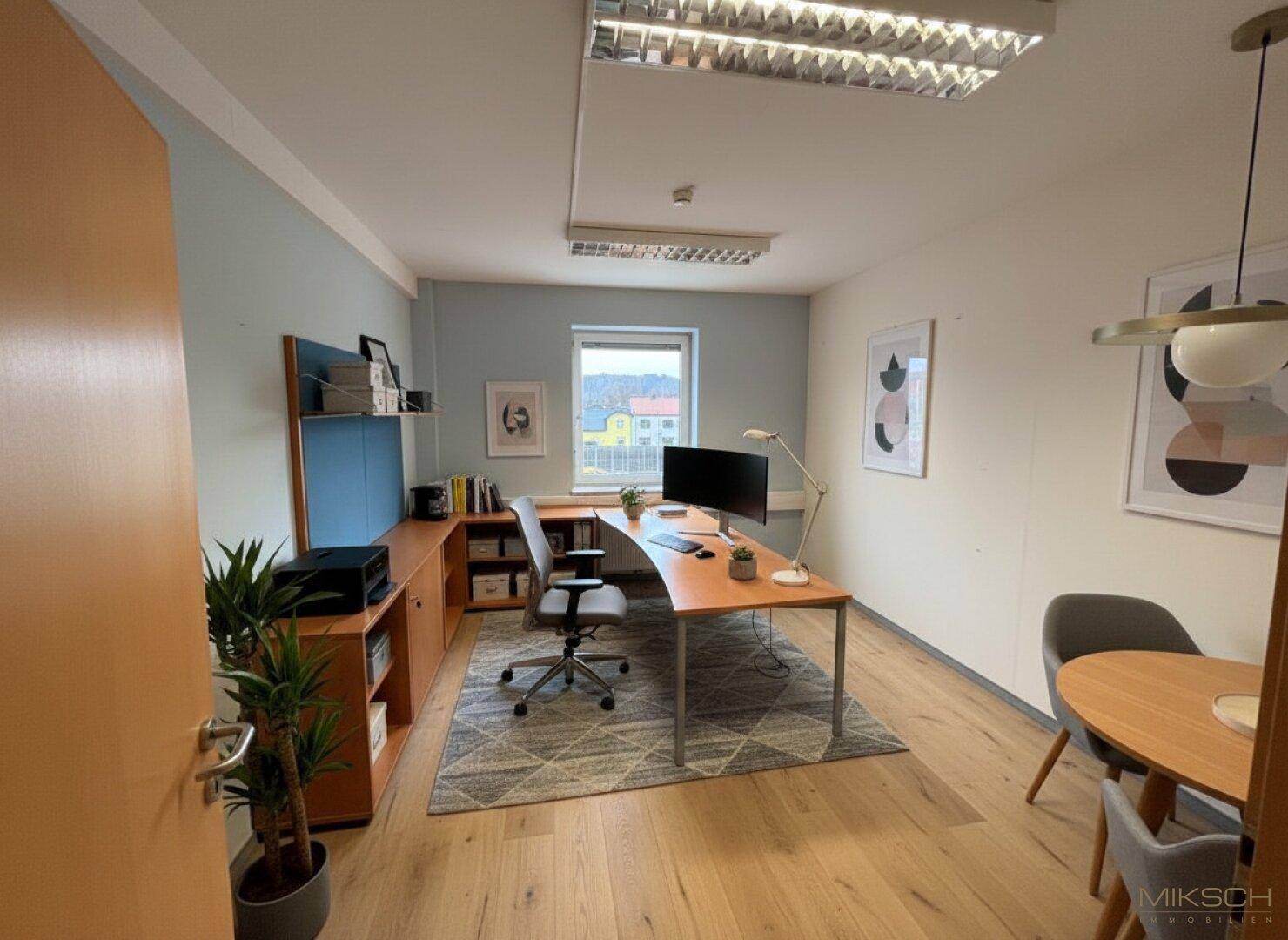 Helles Einzelbüro mit Holzboden, modernem Schreibtisch und einem kleinen Besprechungsbereich.