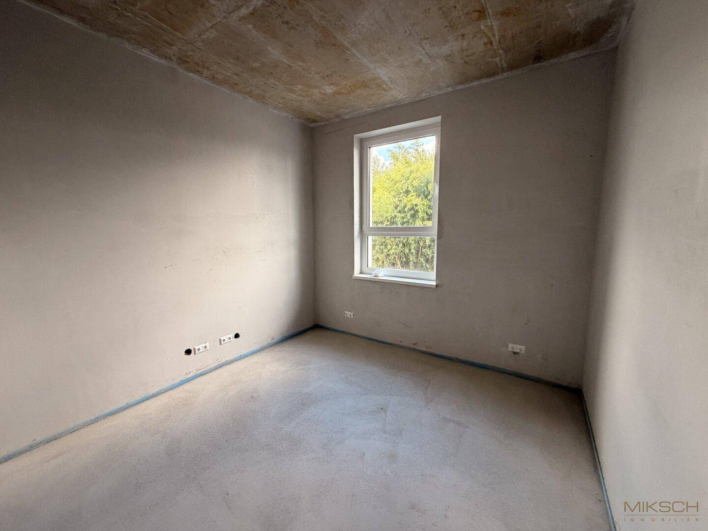 Kleinerer Raum im Rohbauzustand mit einem Fenster und Betonboden.