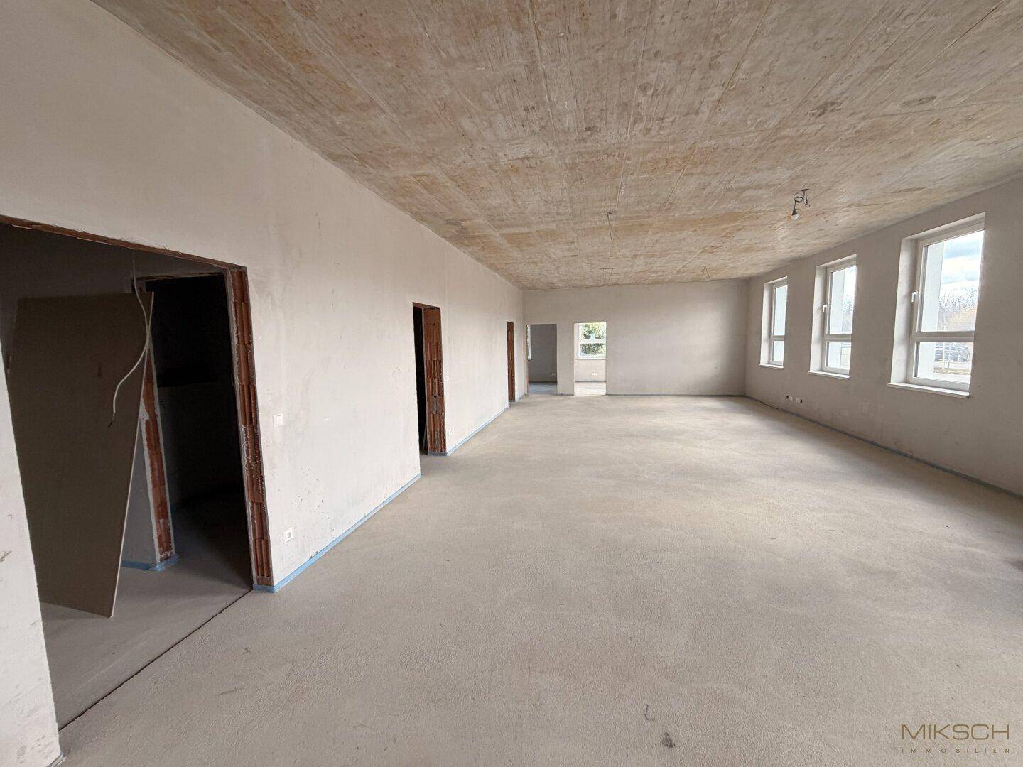 Großer, offener Rohbau mit Betonboden und mehreren Türöffnungen, bereit für die Gestaltung.