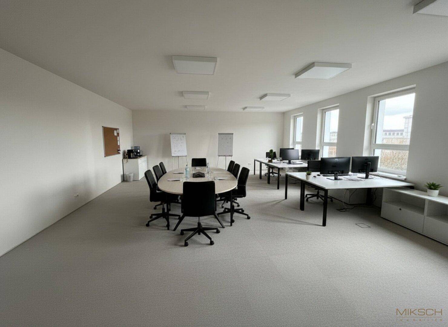 Großes, offenes Büro mit Konferenztisch, mehreren Schreibtischen und viel natürlichem Licht.