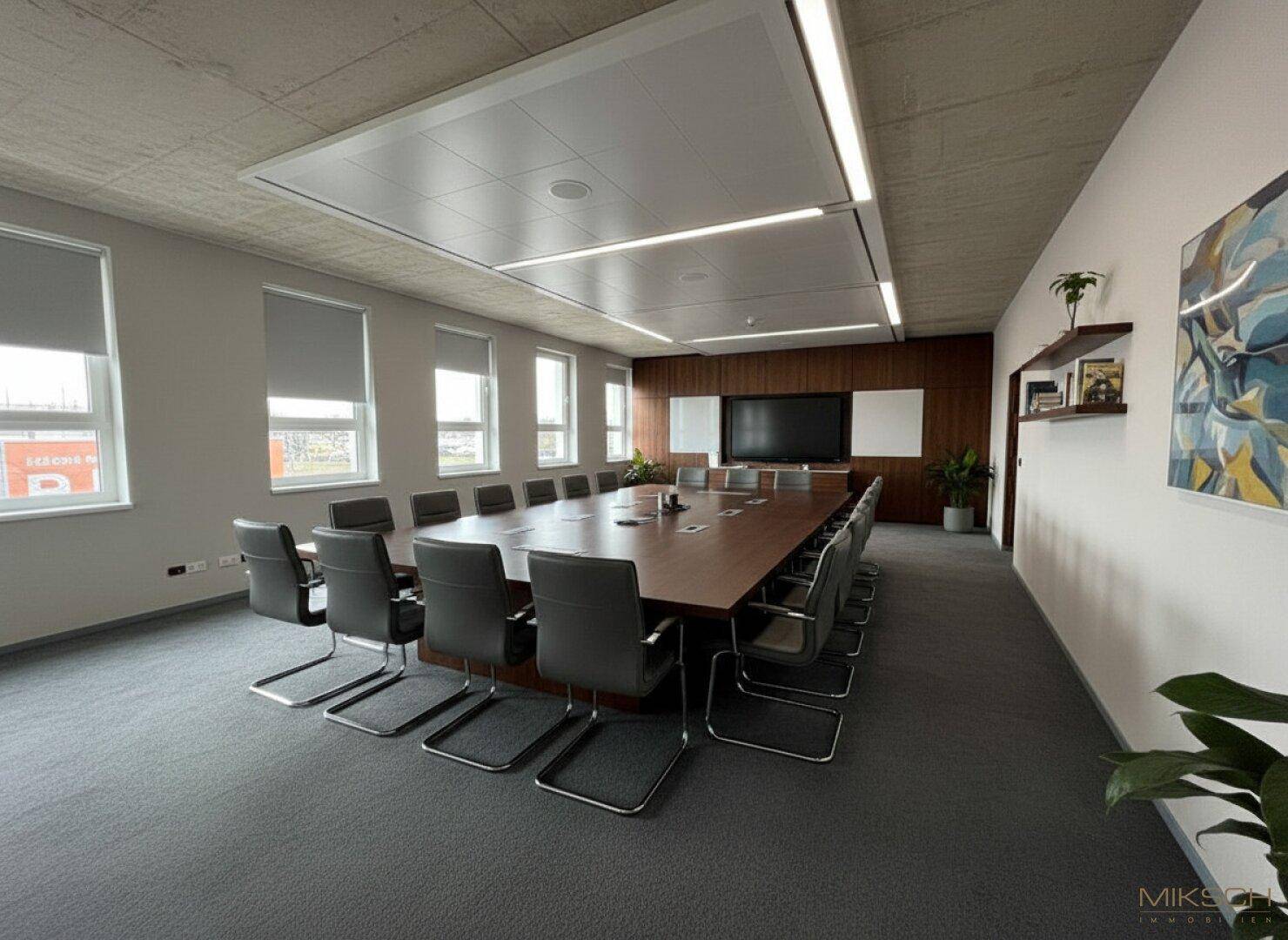Großer, moderner Konferenzraum mit langem Holztisch, vielen Stühlen und integriertem Bildschirm.