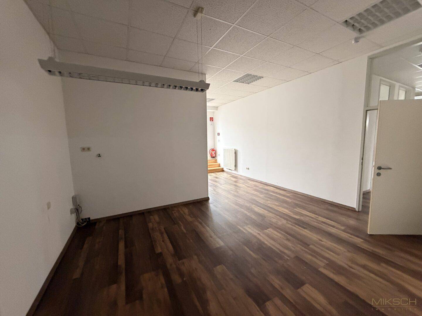 Geräumiger Bürobereich mit dunklem Laminatboden und weißen Wänden, bereit für die Einrichtung.