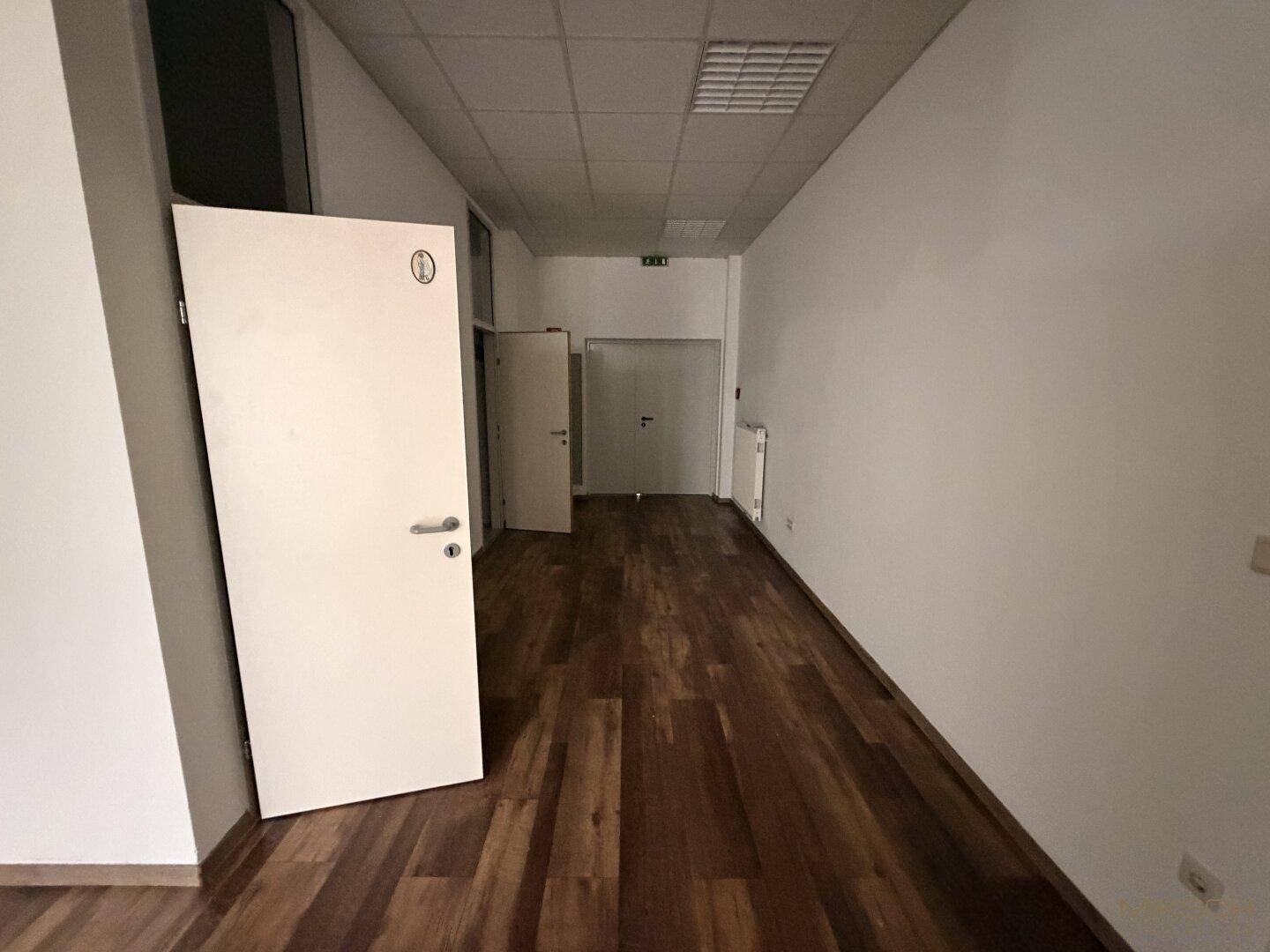 Flur mit dunklem Laminatboden und weißen Wänden, der zu verschiedenen Türen und einem Treppenhaus führt.