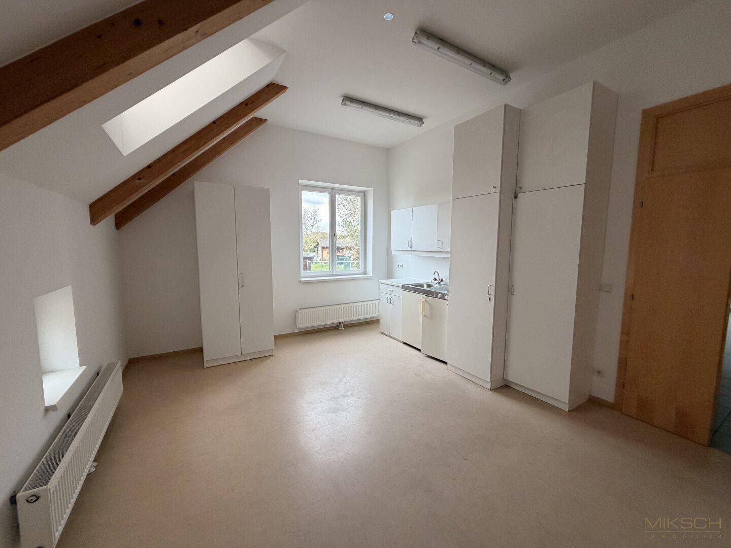 Helle Küchenzeile mit weißen Schränken, Spüle und Kochfeld in einem Raum mit Dachschräge und Fenster.