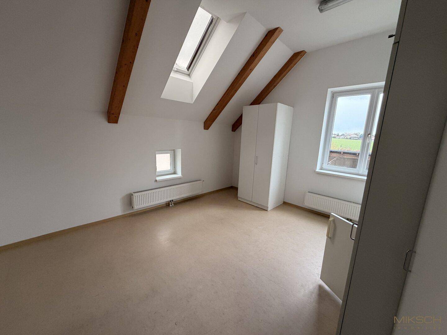 Heller Raum im Dachgeschoss mit Dachfenster, Holzbalken und einem Schrank, ideal als Büro oder Lager.
