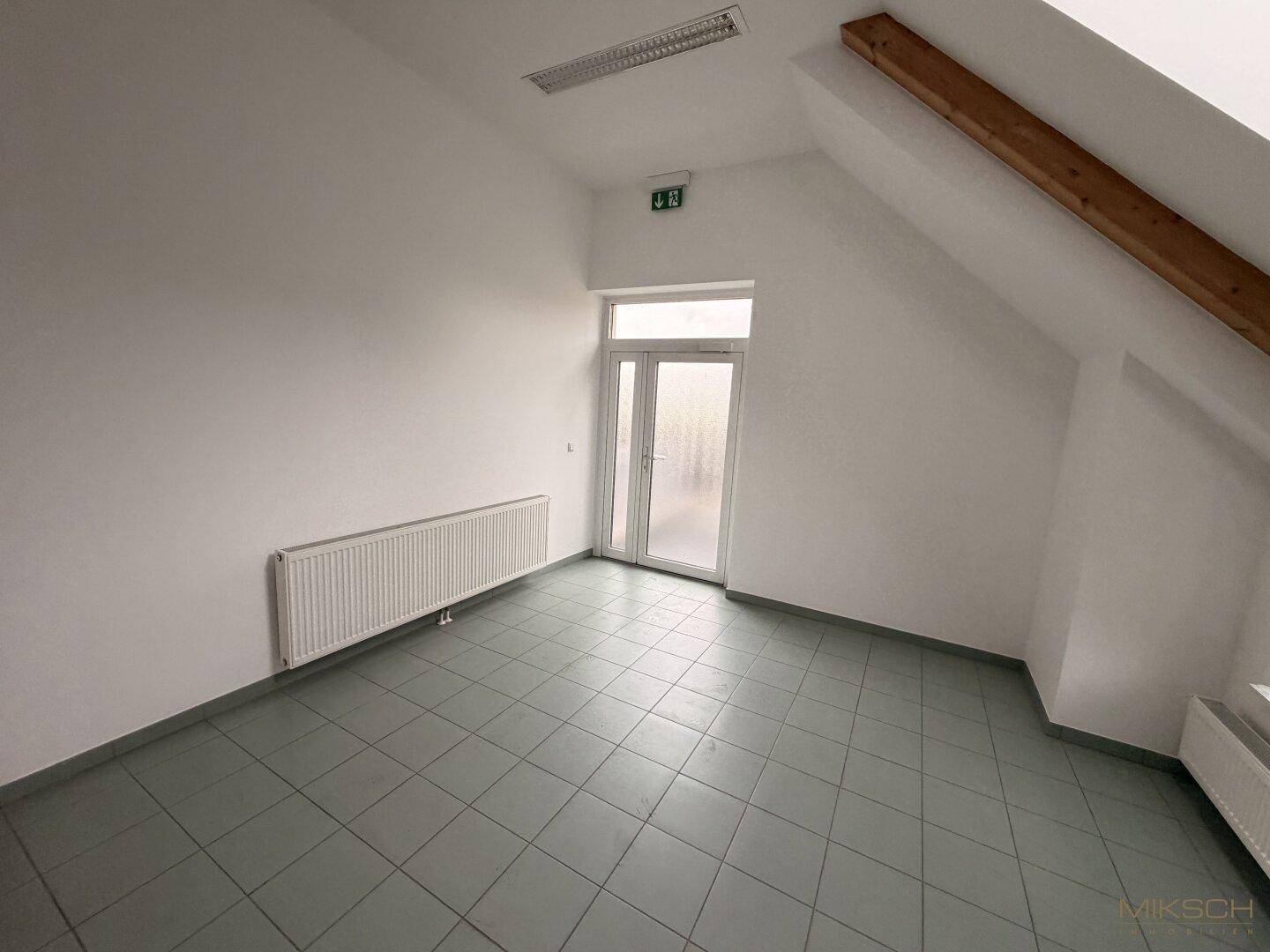 Heller Flur mit Fliesenboden, Dachschräge und einer Glastür, die den Zugang zum Außenbereich ermöglicht.