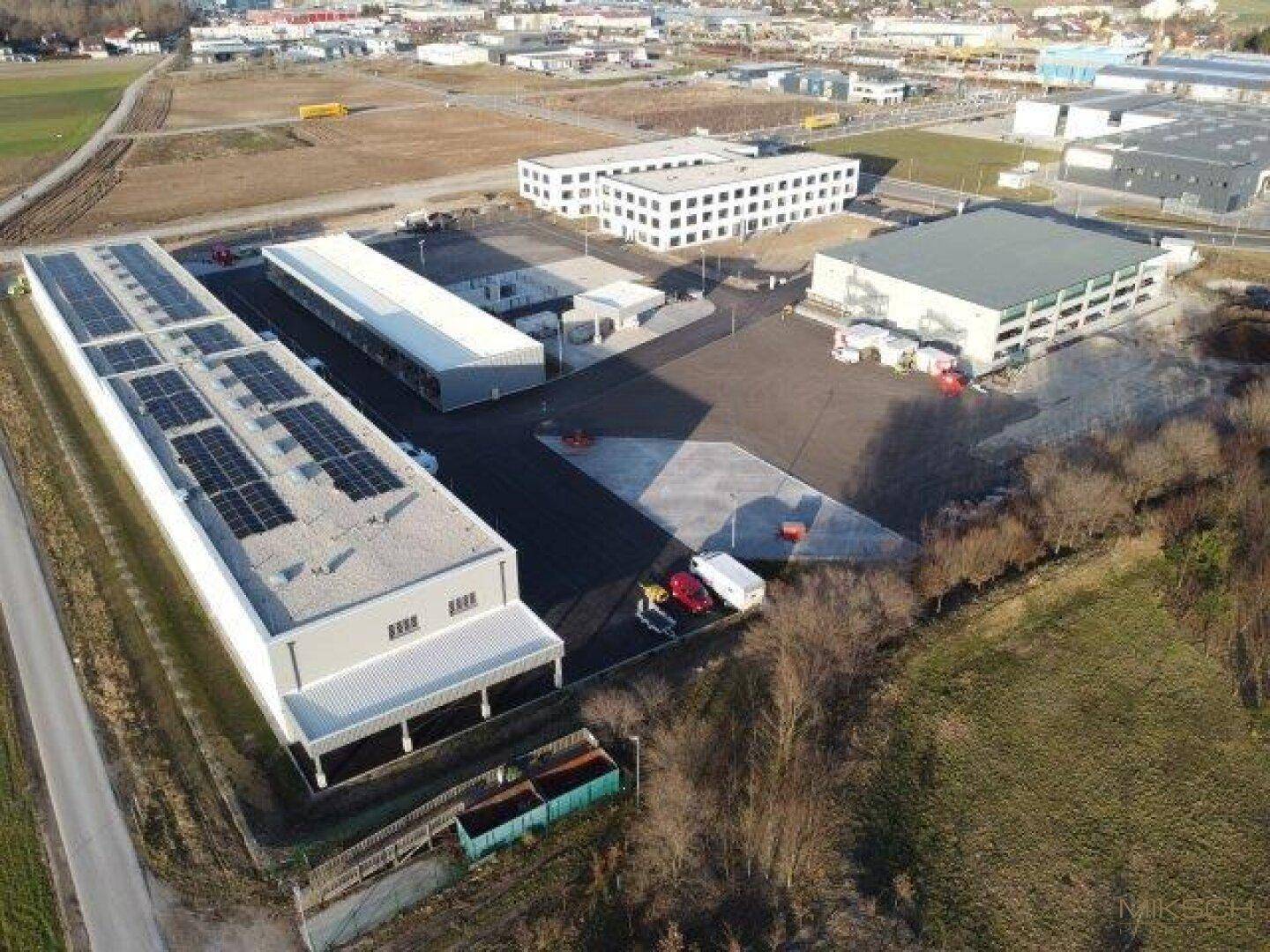 Luftaufnahme eines modernen Gewerbeparks mit mehreren Gebäuden, Parkplätzen und Solaranlagen auf den Dächern.