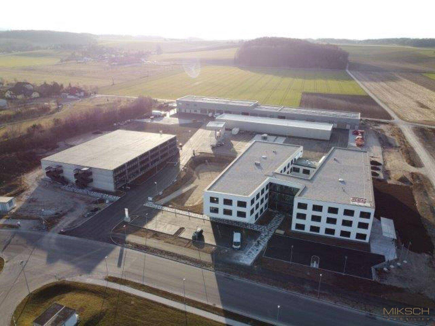 Weitläufige Luftaufnahme eines Gewerbegebiets mit mehreren Gebäuden, umgeben von Feldern und Natur.