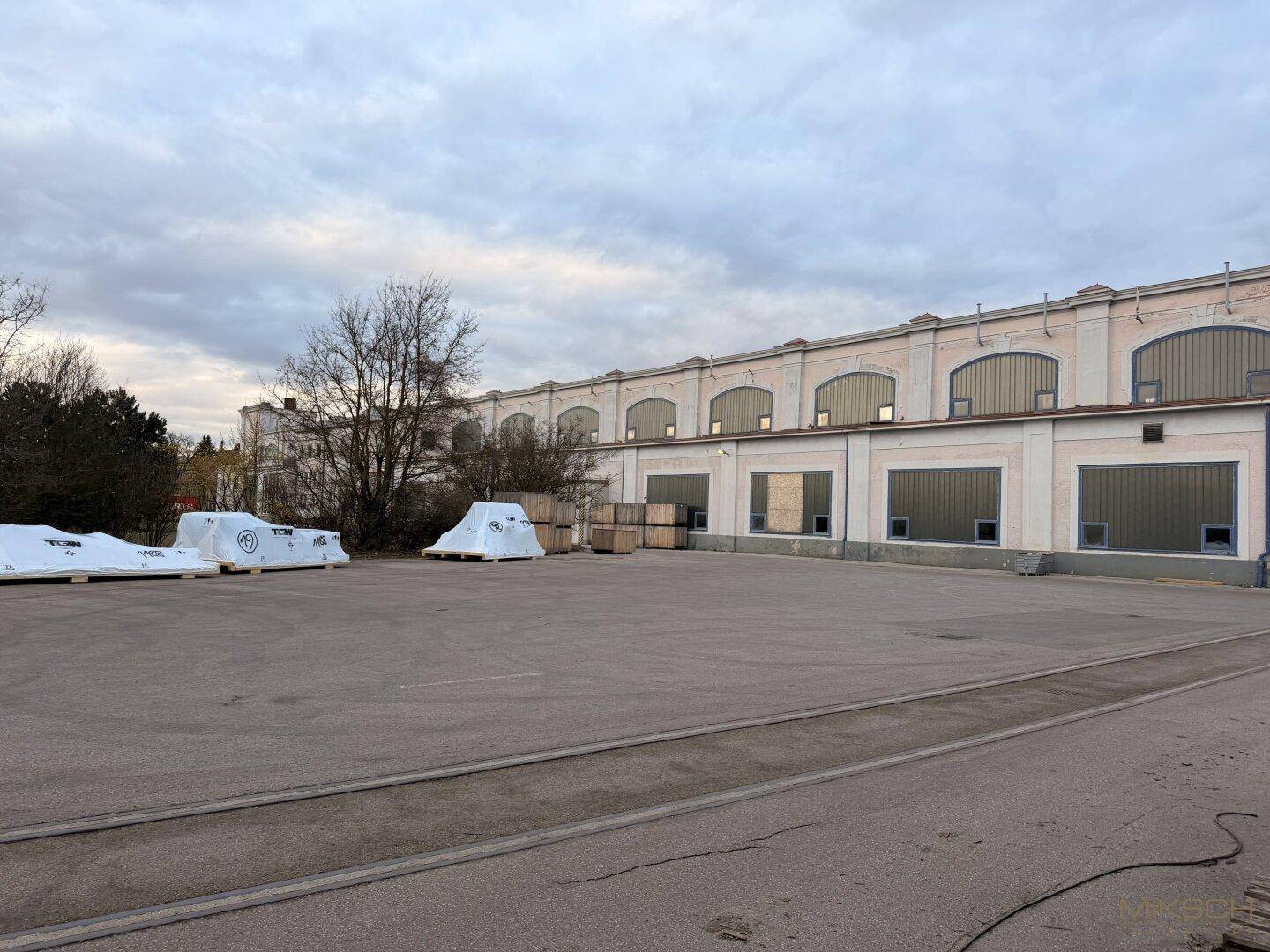 Fassade eines Industriegebäudes mit Bogenfenstern und einem großen asphaltierten Hof, ideal für Logistik.