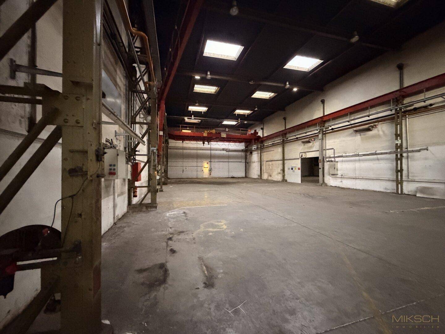 Innenansicht eines Teils der Industriehalle mit Betonboden, hohen Decken und einem roten Brückenkran.