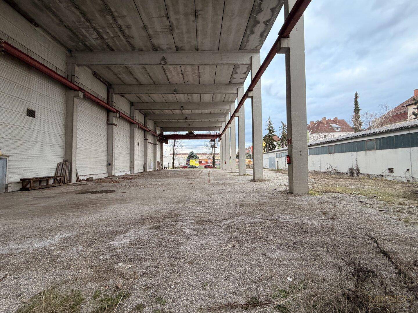 Außenbereich unter einem Betonüberhang mit tragenden Säulen und einem Schotterboden, bietet Schutz.