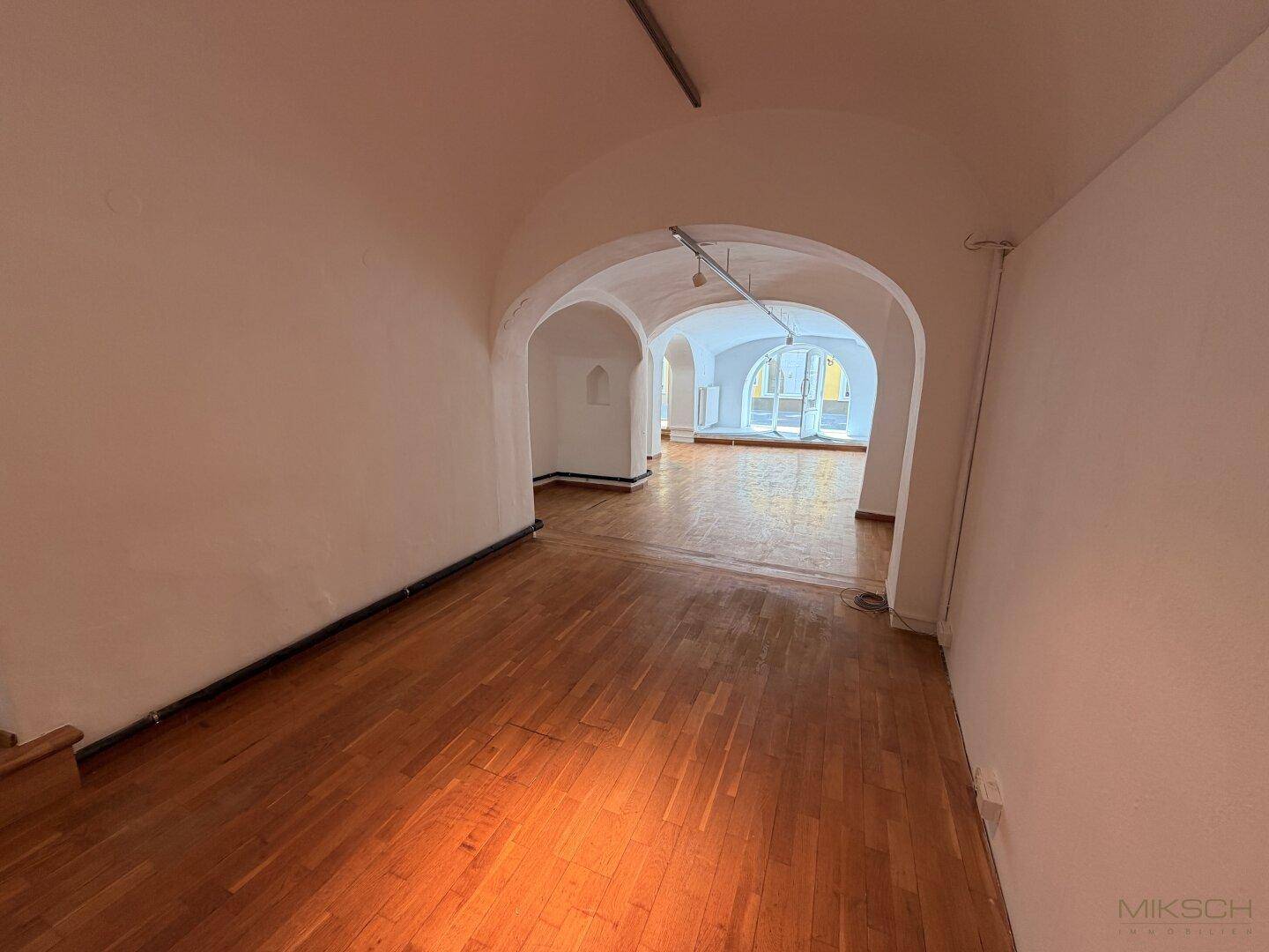 Langer Gewerberaum mit Holzboden, gewölbten Decken und mehreren Bögen, die zu weiteren Bereichen führen.