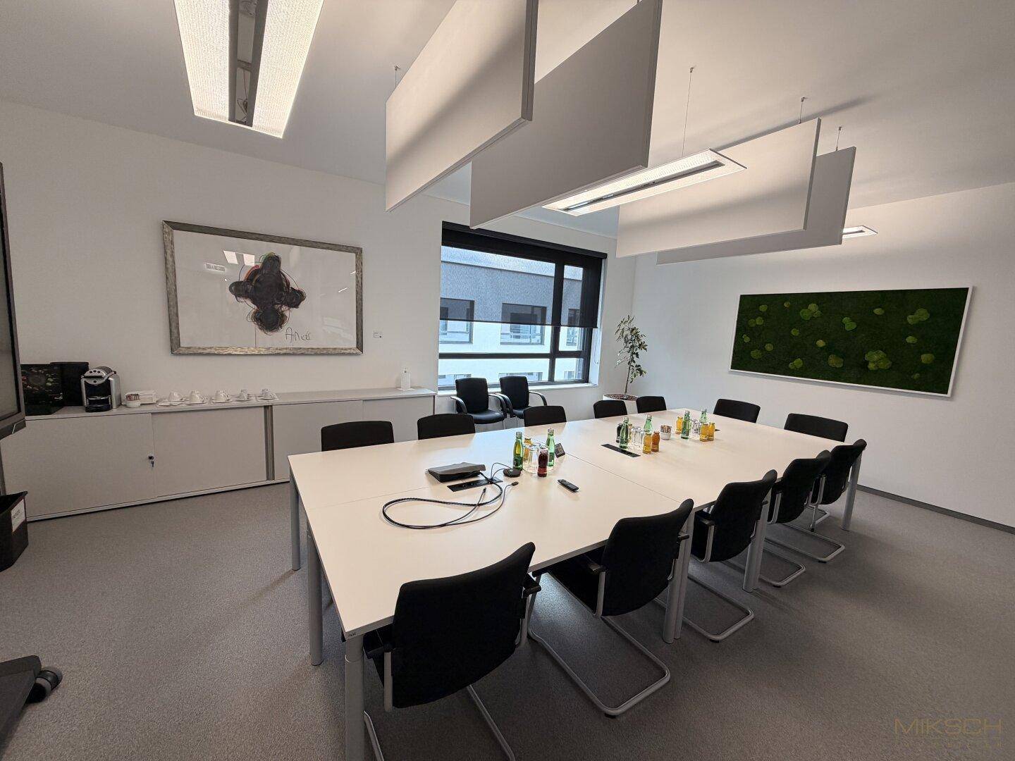 Großer Konferenzraum mit modernem Tisch, schwarzen Stühlen, Fenster und schallabsorbierenden Deckenpaneelen.