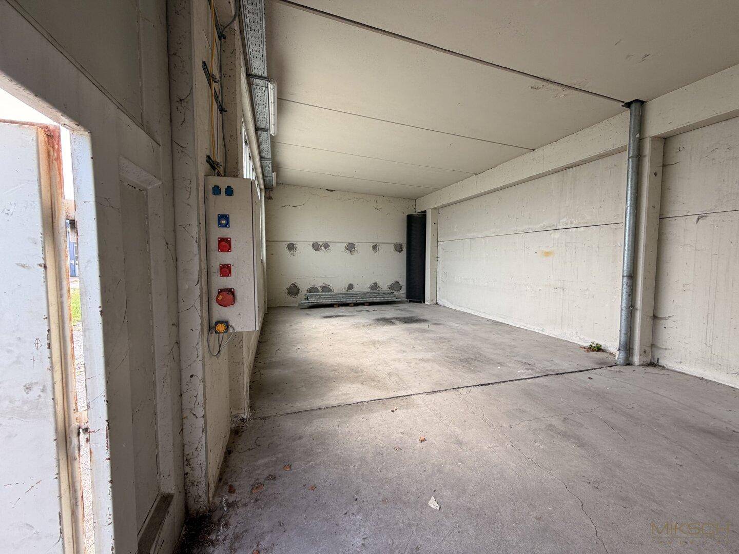 Heller Lagerraum mit Betonboden, hohen Decken und sichtbaren Installationen, ideal für gewerbliche Nutzung.