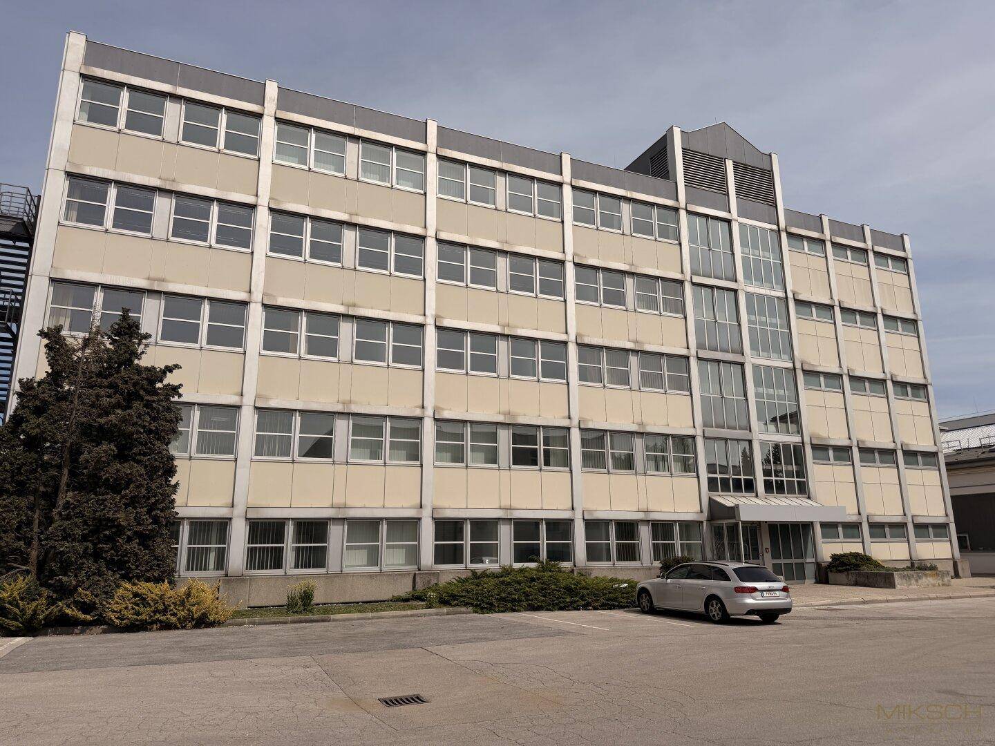 Mehrstöckiges Geschäftsgebäude mit zahlreichen Fenstern und einer modernen Fassade, davor ein Parkplatz.