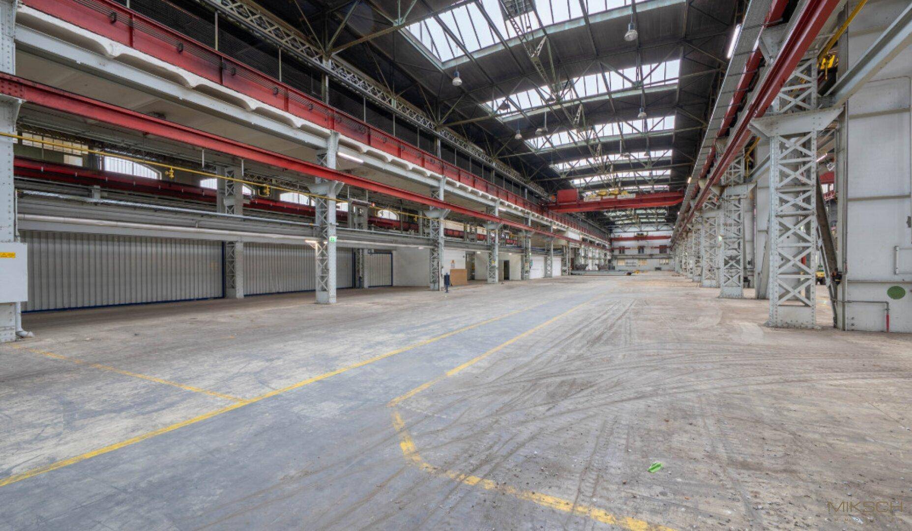 Weitläufige Industriehalle mit Tageslicht durch Oberlichter und robustem Betonboden, bereit zur Nutzung.