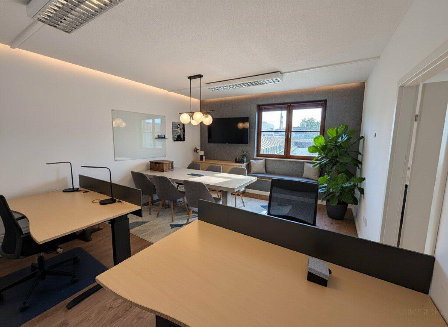 Modernes Büro mit flexiblen Arbeitsbereichen, einem Besprechungstisch und großen Fenstern für viel Tageslicht.