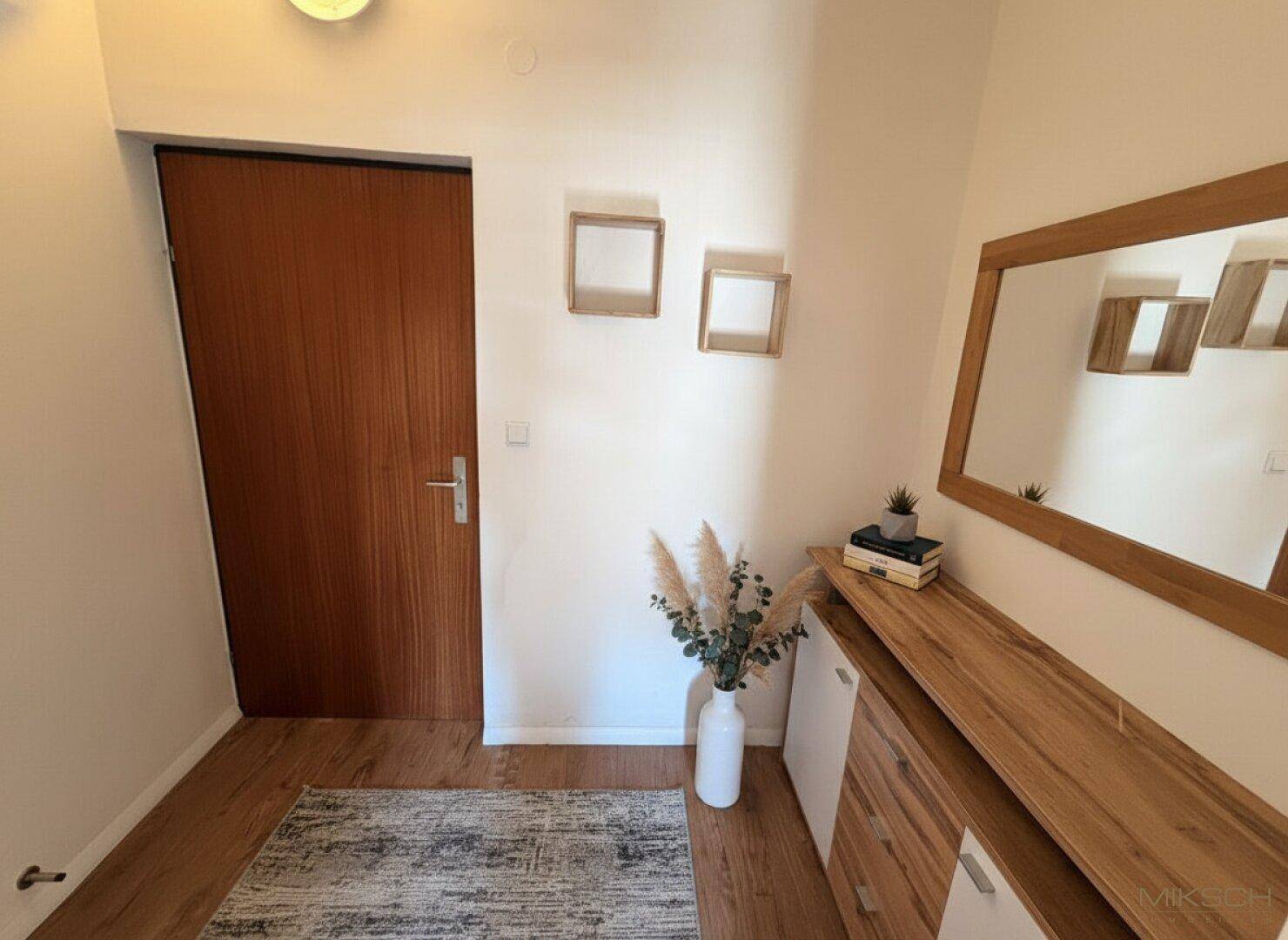Heller Flur mit Holzboden, einer eleganten Kommode und einem großen Spiegel, der den Raum optisch erweitert.