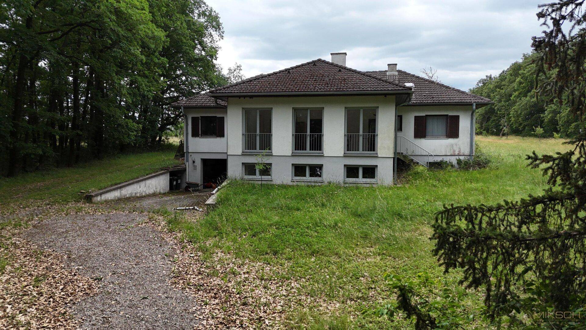 Vorderansicht des Hauses mit großen Fenstern und Balkonen, umgeben von üppigem Grün und Bäumen.