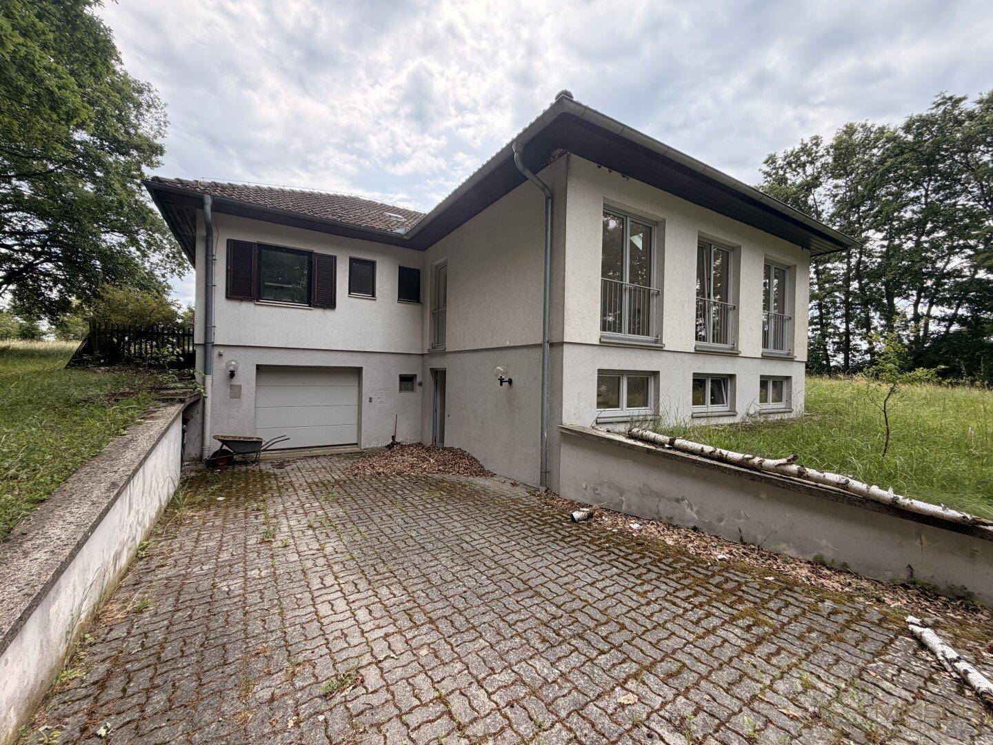 Außenansicht des Hauses mit integrierter Garage und gepflasterter Zufahrt unter bewölktem Himmel.