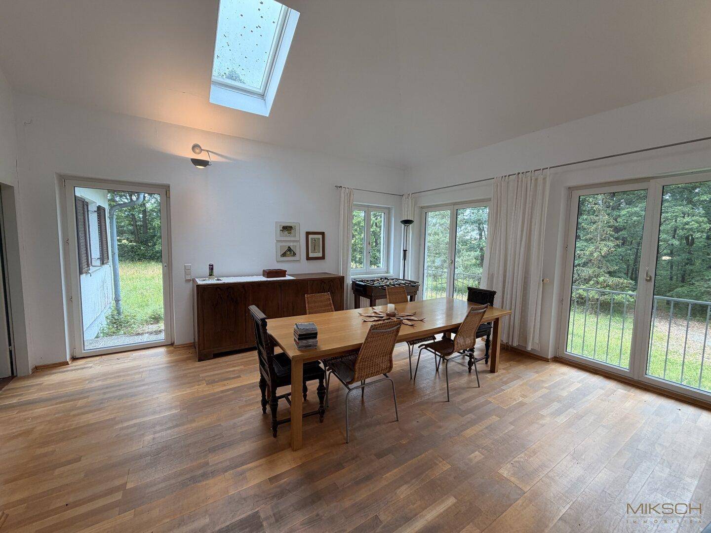 Heller Essbereich mit Holzboden, großem Esstisch und Zugang zum Garten, ergänzt durch ein Dachfenster.