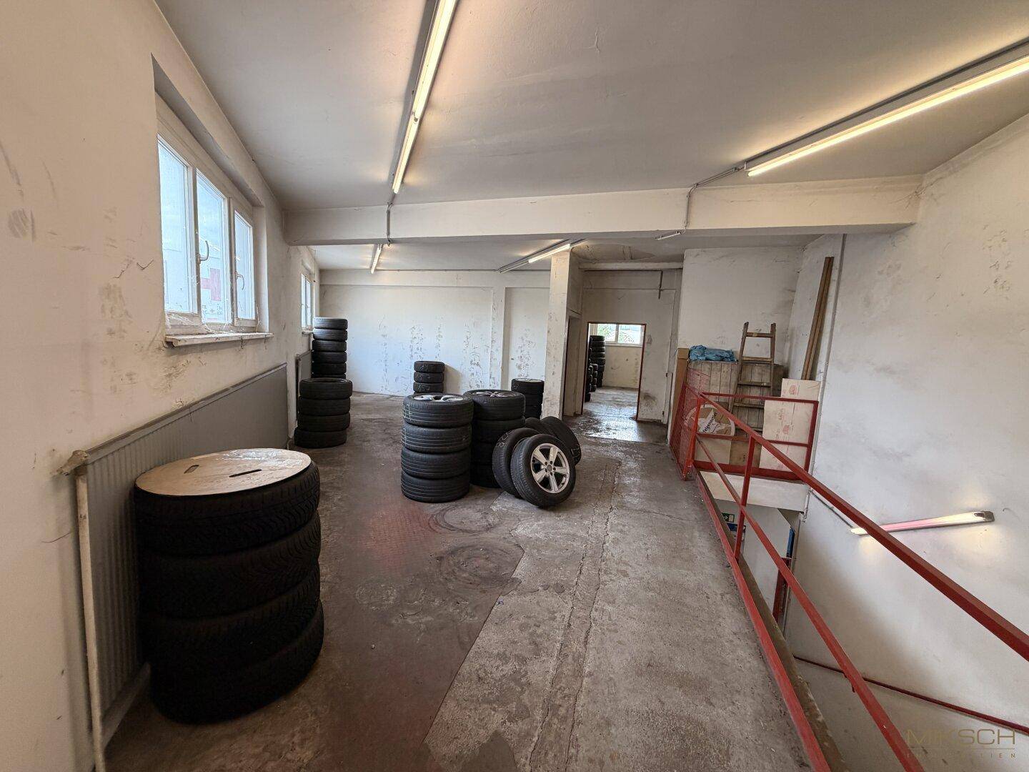 Ein Lagerbereich im Obergeschoss mit gestapelten Reifen, Fenstern und einem Treppenabgang.