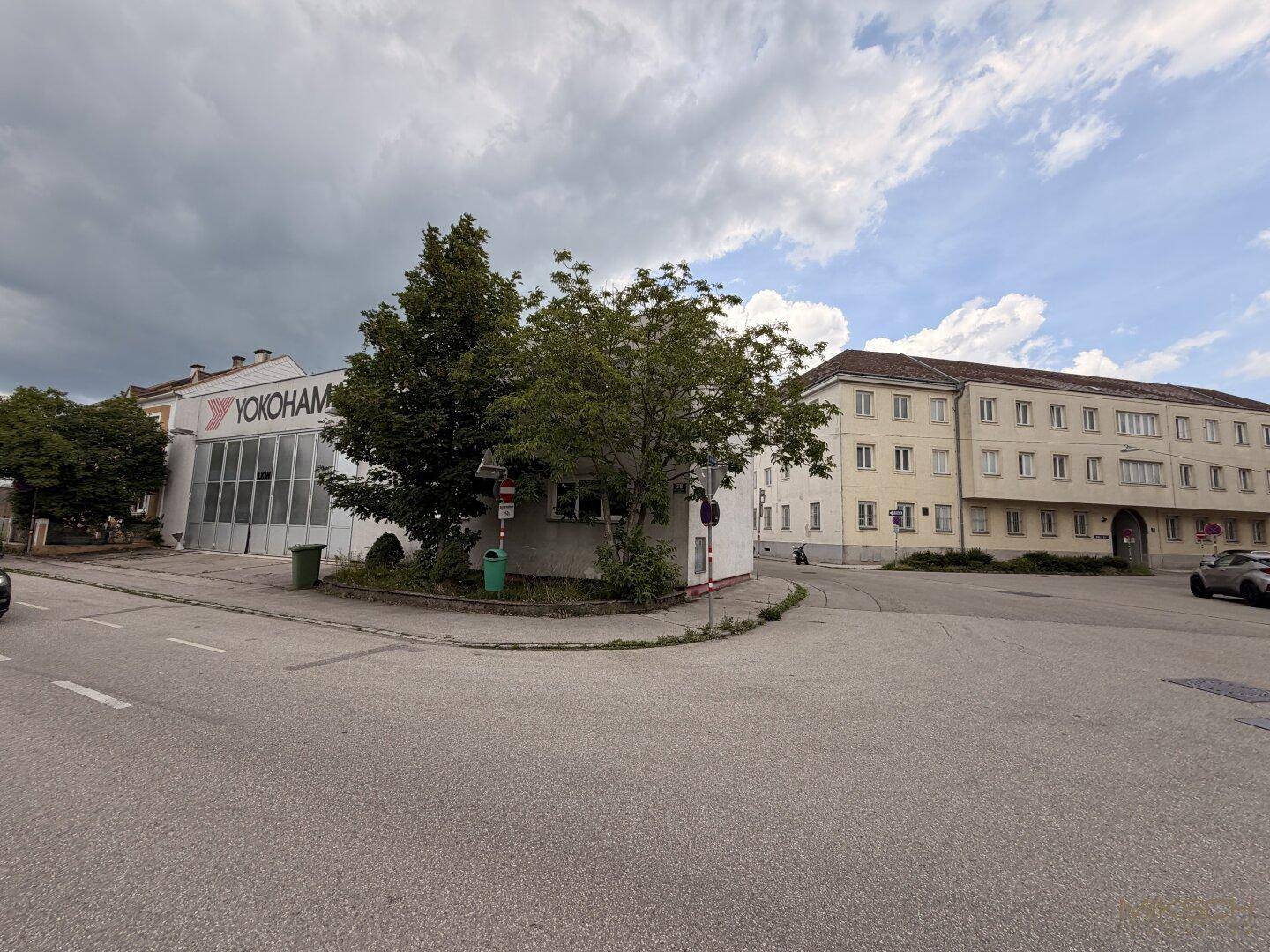 Die Außenansicht des Gewerbegebäudes von der Straße, umgeben von Bäumen und anderen Gebäuden.