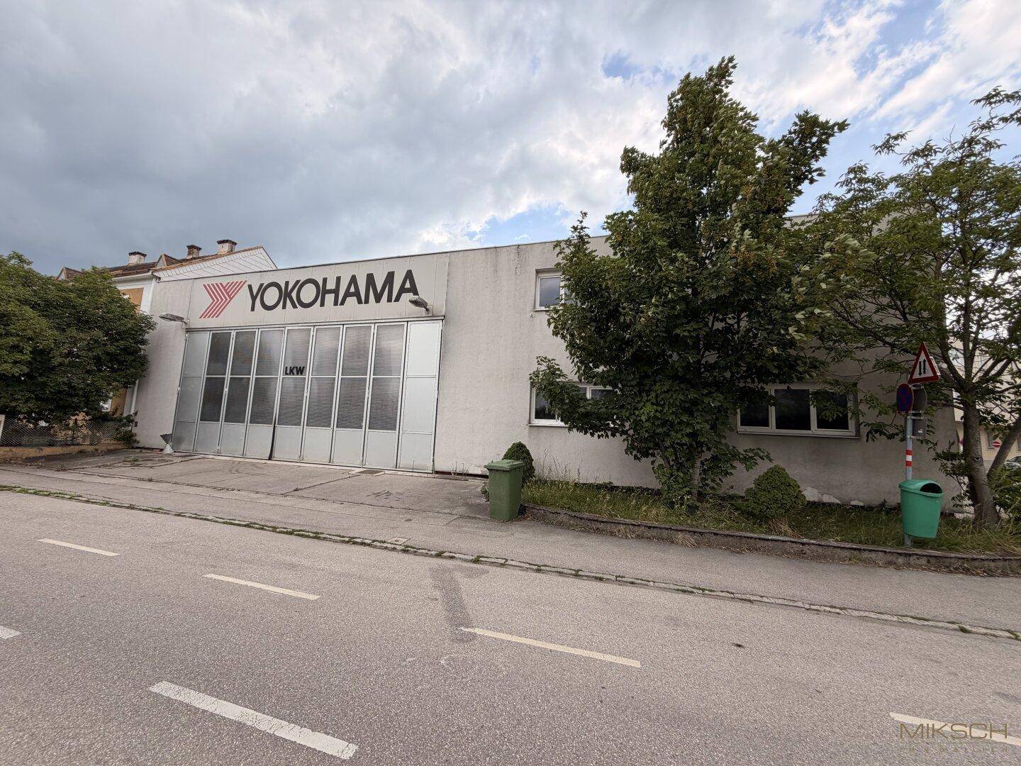Seitenansicht des Gewerbegebäudes mit Yokohama-Logo, Bäumen und einer Zufahrt von der Straße.