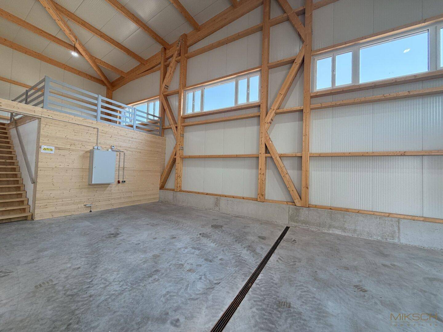 Innenansicht einer modernen Lagerhalle mit Betonboden, hohen Fenstern und Holzkonstruktion.