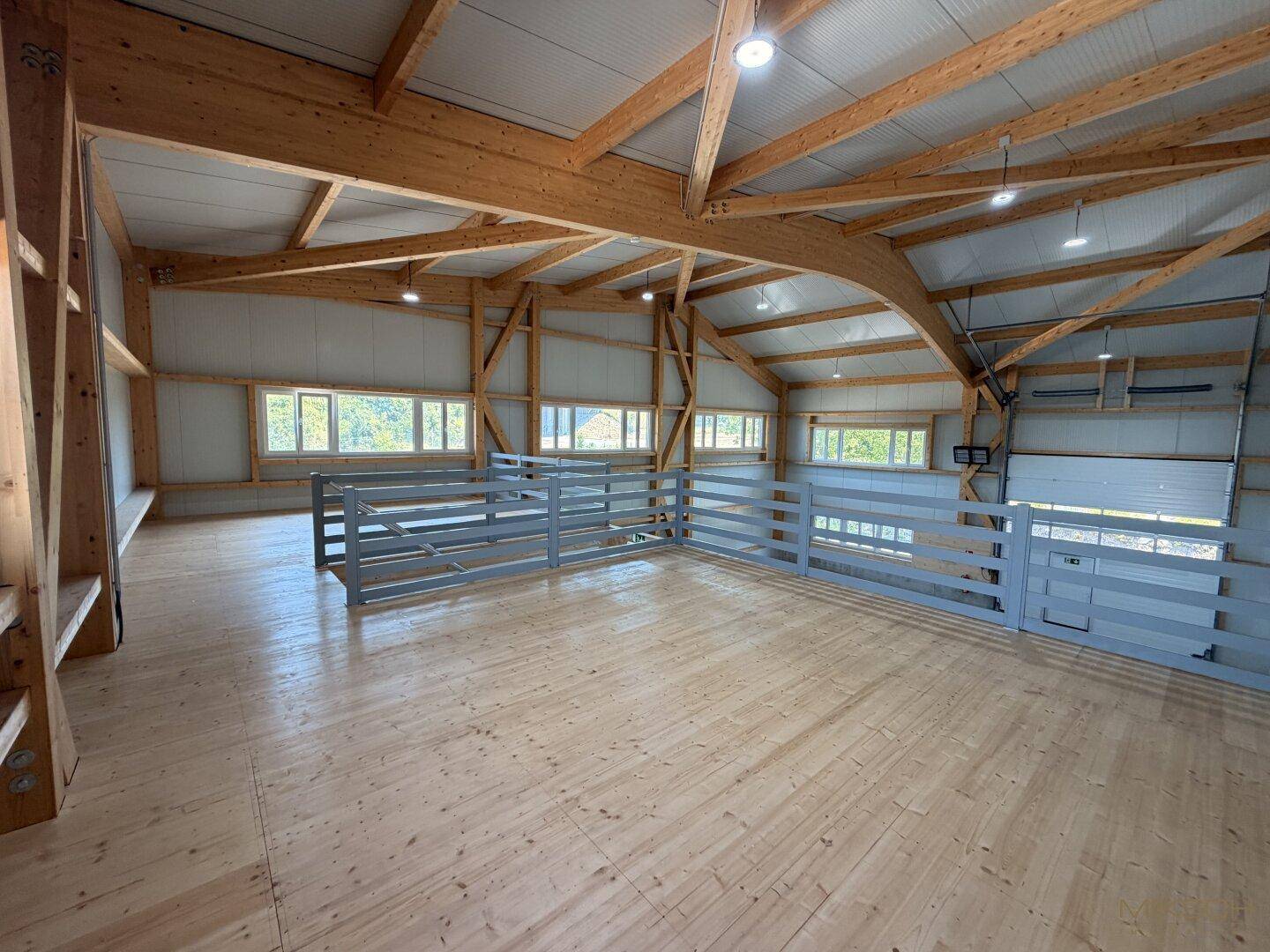 Obergeschoss einer Halle mit Holzboden, grauen Geländern und sichtbarer Holzkonstruktion.