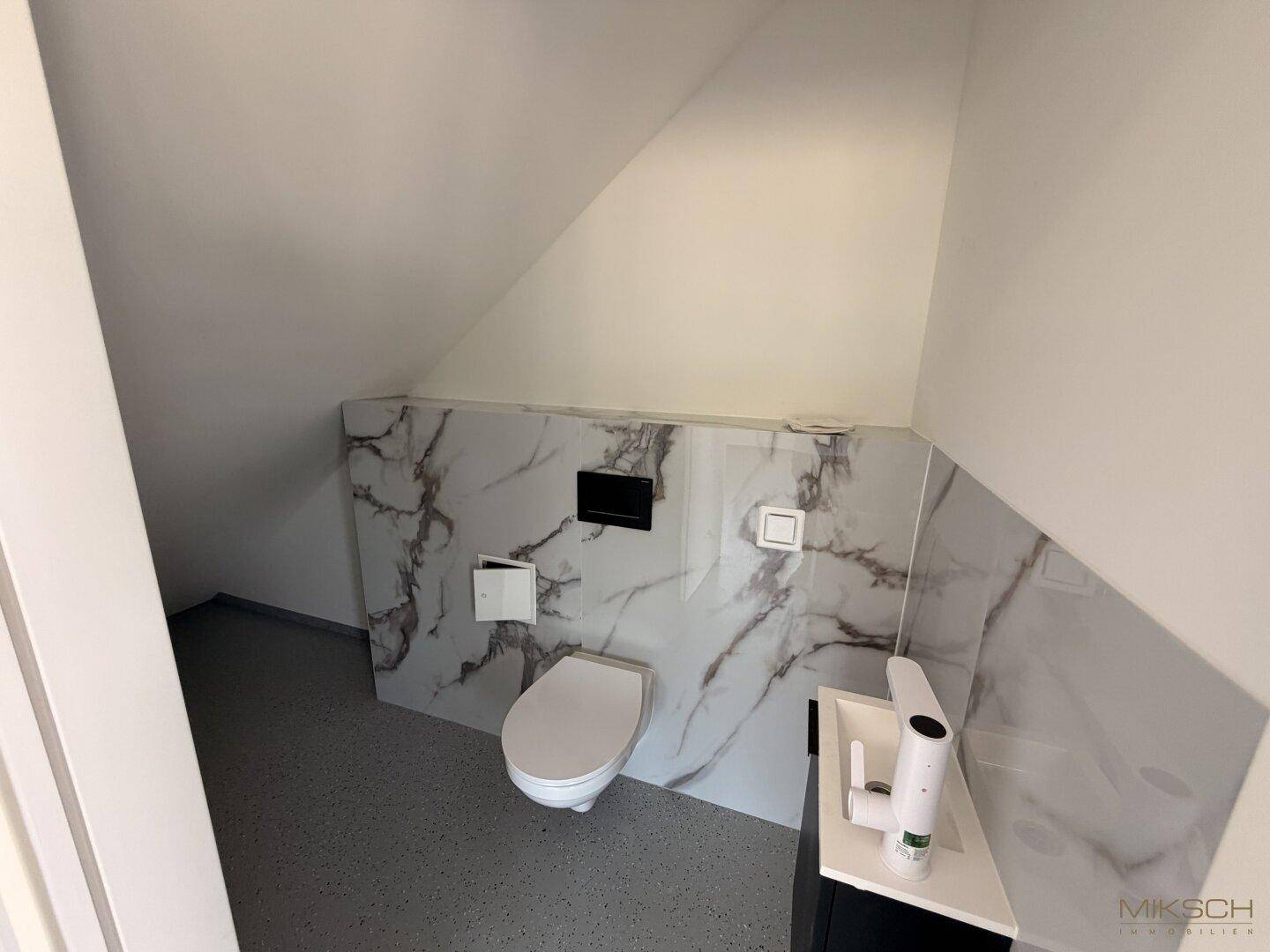 Modernes Gäste-WC mit Marmoroptik-Fliesen, wandhängendem WC und Dachschräge.