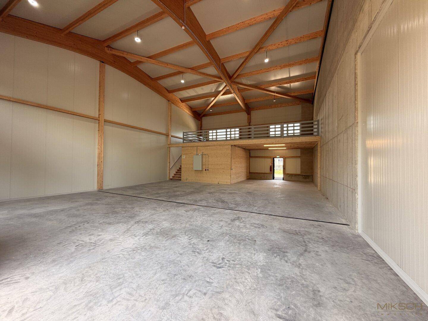 Weitläufige Lagerhalle mit Holzkonstruktion, Betonboden und einer erhöhten Galerie, ideal für gewerbliche Nutzung.