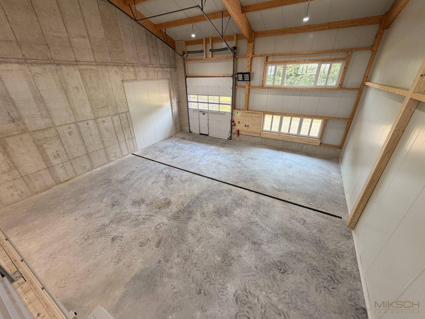 Große, leere Lagerfläche mit Betonboden, hohen Decken und einem Sektionaltor, ideal für Logistik.