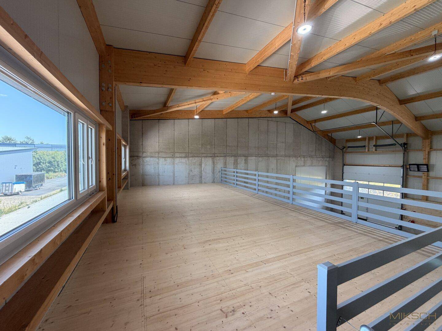 Helle Galerieebene mit Holzfußboden und großen Fenstern, die einen Blick nach draußen ermöglichen.
