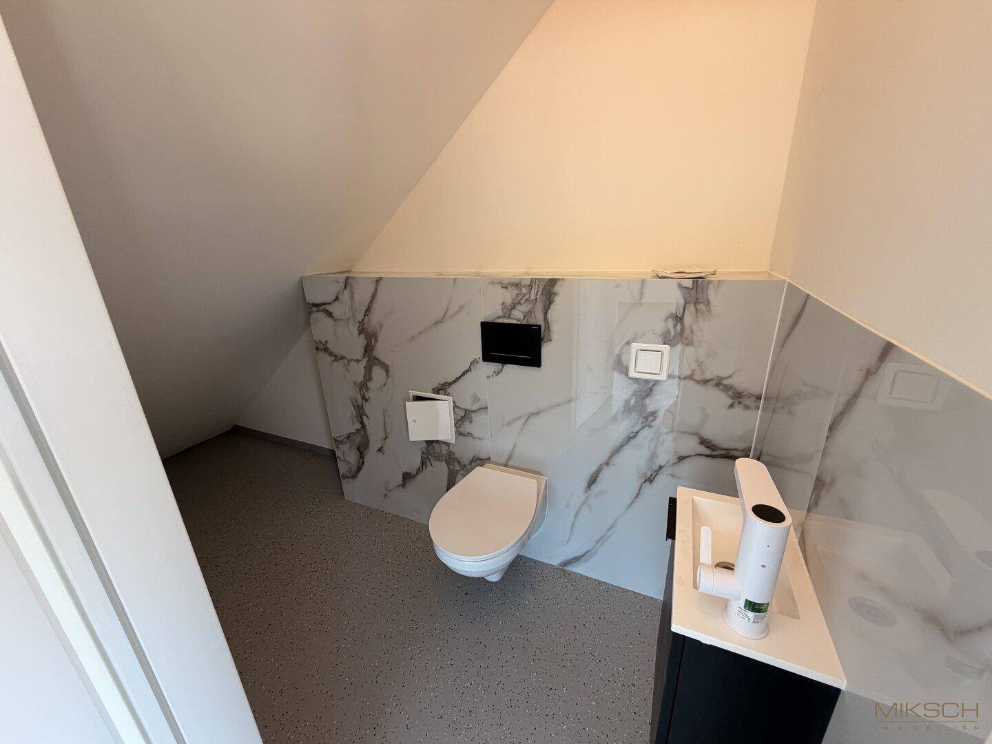 Kleiner Toilettenraum mit modern gefliesten Wänden in Marmoroptik und Dachschräge.