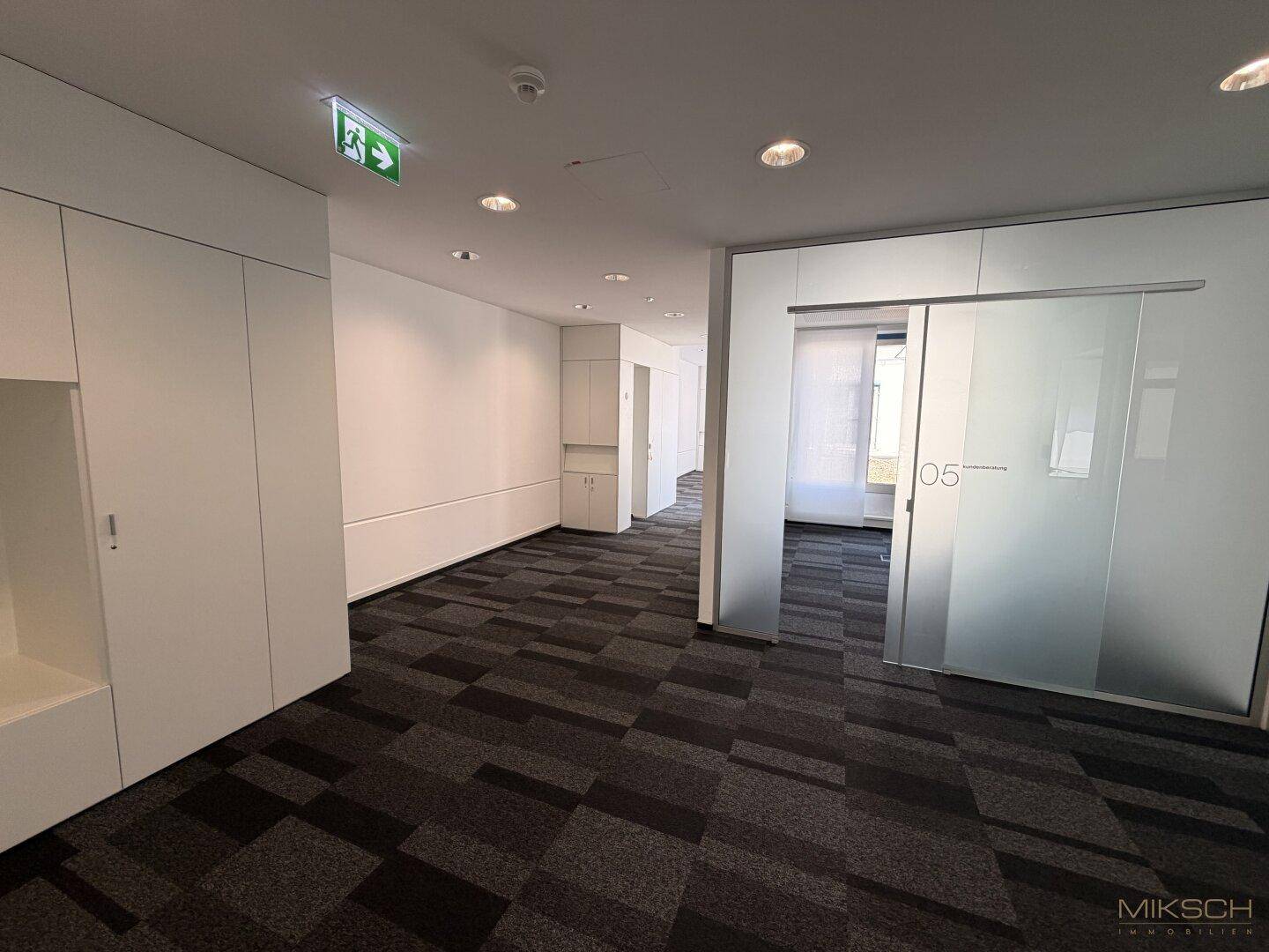 Moderner Bürogang mit gemustertem Teppichboden, Einbauschränken und einer Milchglas-Schiebetür.