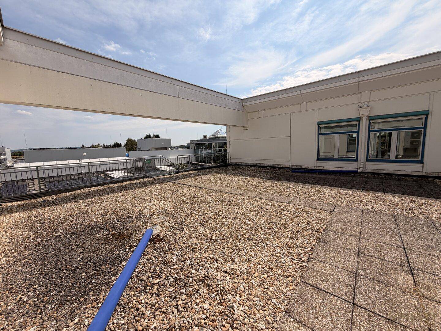 Weitläufige Dachterrasse mit Kiesbelag und Blick auf umliegende Gebäude unter blauem Himmel.