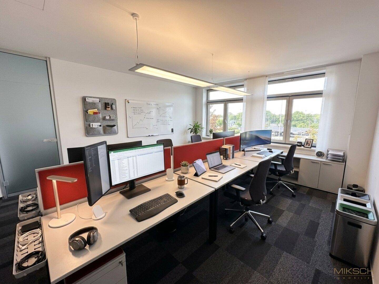 Modernes Großraumbüro mit mehreren voll ausgestatteten Arbeitsplätzen und großen Fenstern.