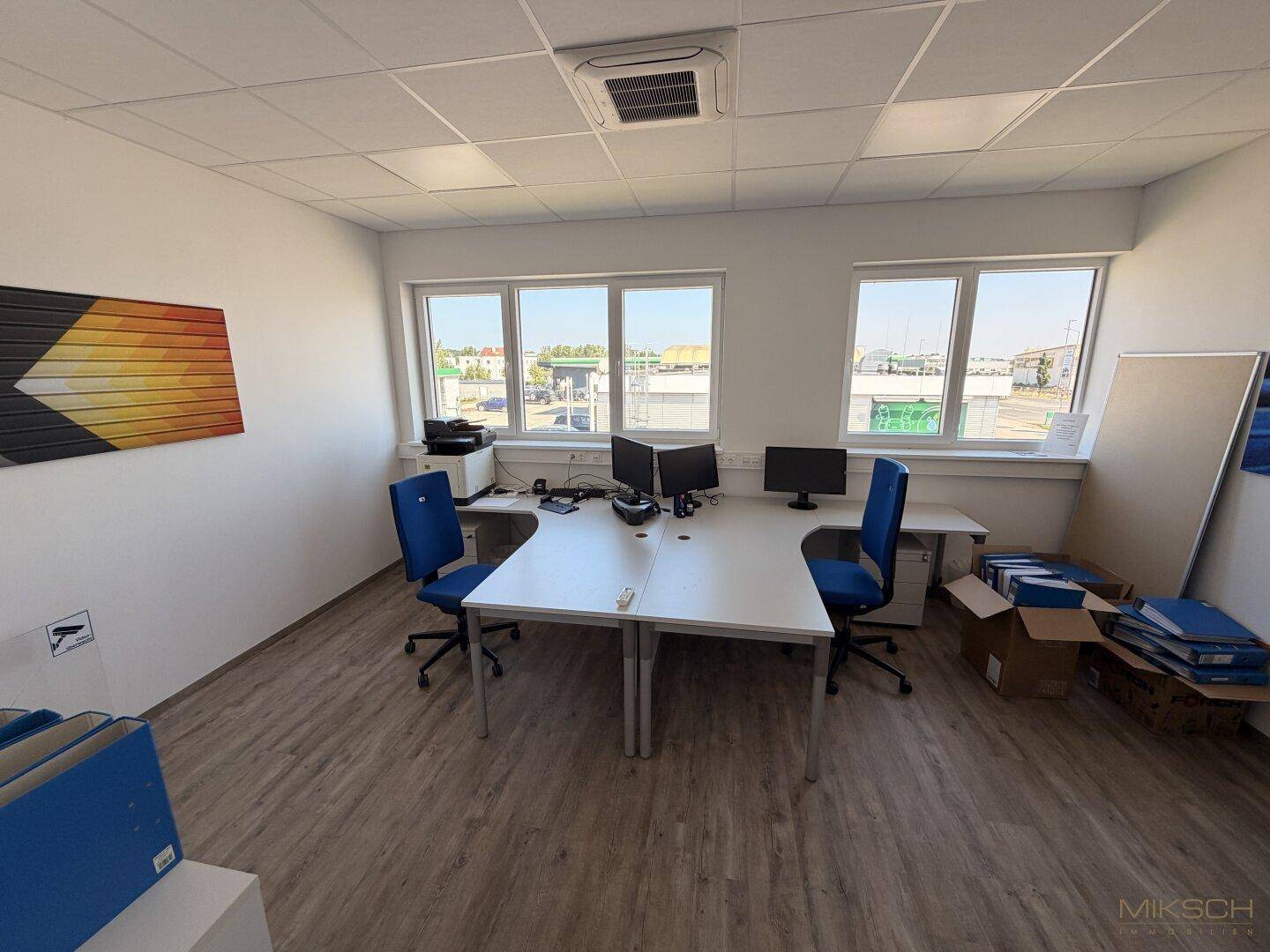 Funktionales Büro mit zwei Schreibtischen, Bürostühlen und Blick durch die Fenster auf das Gelände.