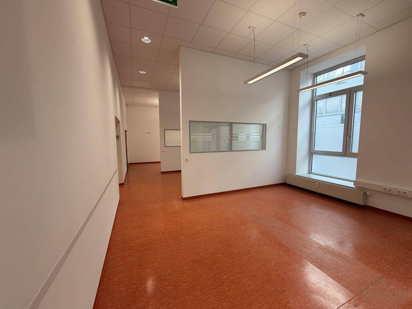 Heller Büroraum mit großen Fenstern, die viel Tageslicht hereinlassen, und orangefarbenem Boden.