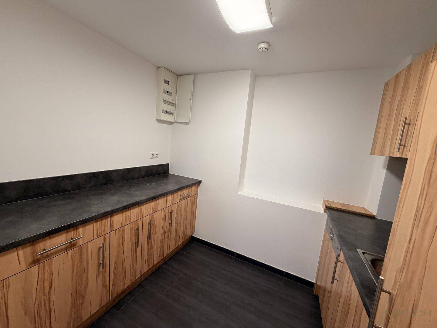 Funktionale Küchenzeile mit Holzschränken, dunkler Arbeitsplatte und dunklem Fliesenboden.
