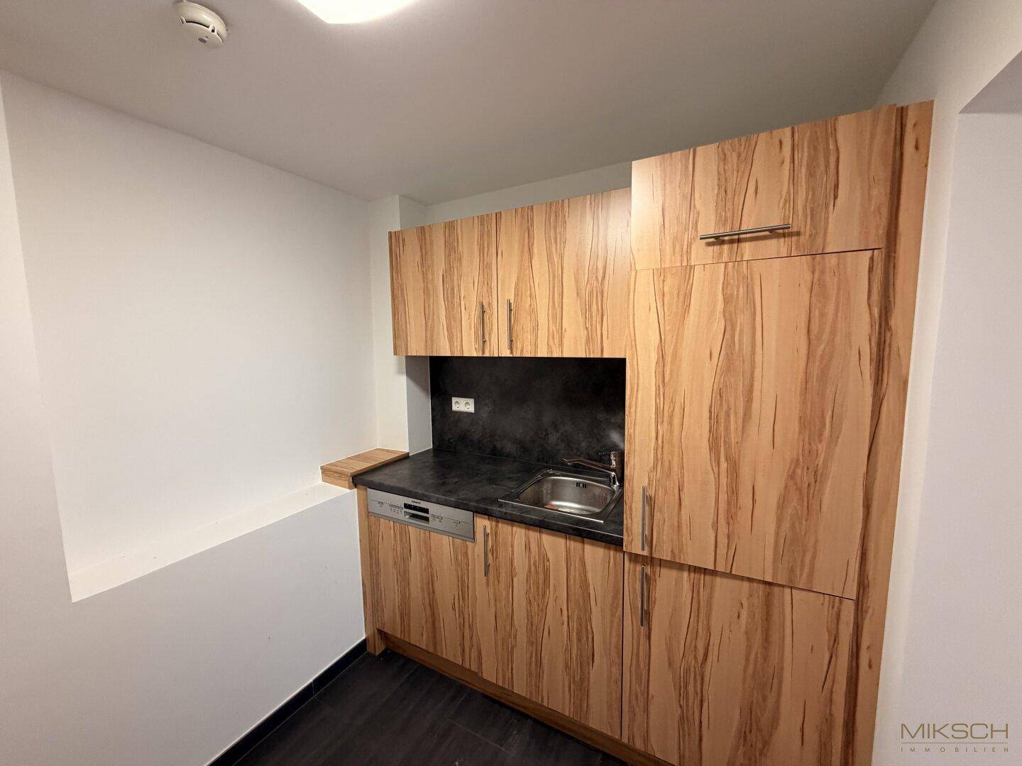 Kleine Küchenzeile mit integriertem Geschirrspüler, Spüle und Holzmaserung an den Schränken.